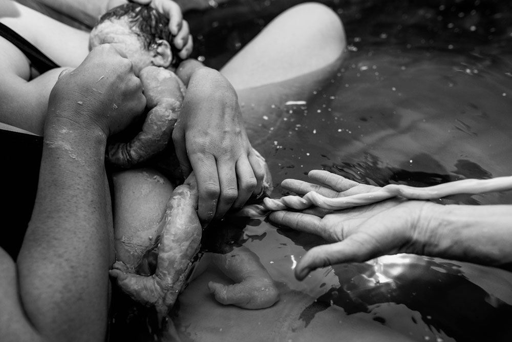 Midwife showing newborn baby's umbilical cord in birthing tub during a home birth story