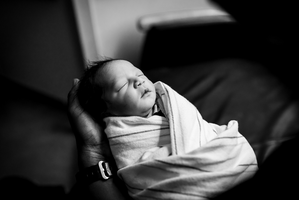 Baby boy sleeps in dads hands while wrapped in a blanket in Salt Lake City, Utah