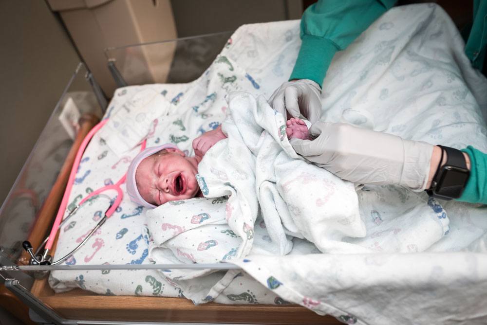 Newborn baby cries while nurse does his first newborn check