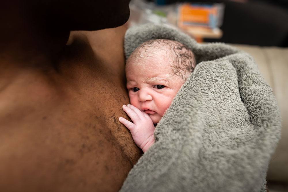 Twin B lies on daddy's chest after birth with his eyes open