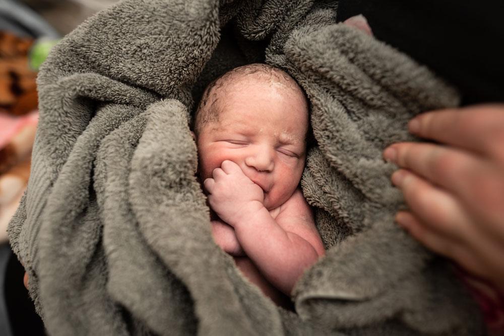 Twin B sucks his thumb while wrapped in a green towel