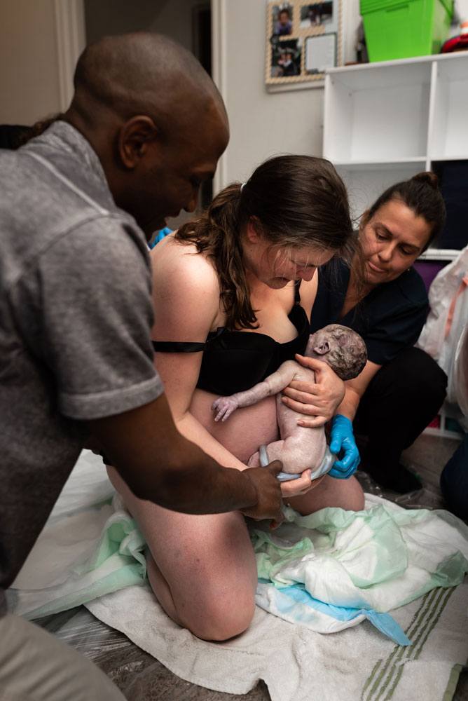 Mom holds Twin A in her arms as midwife and husband help unwrap his cord from around his body