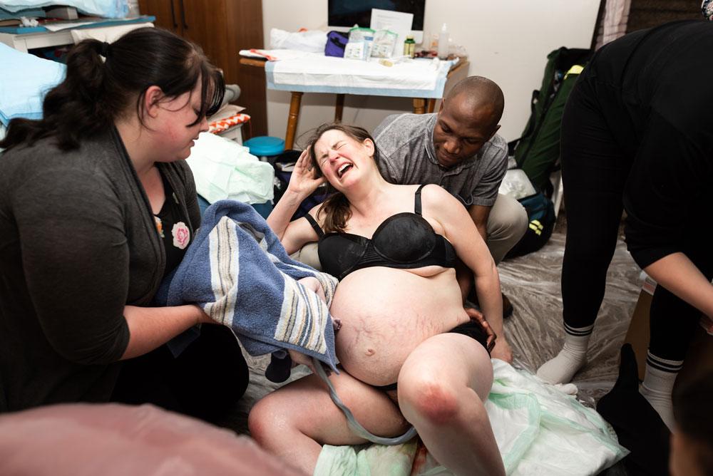 Mother leans on her husband as she waits for the birth of twin B during a home birth in salt lake city