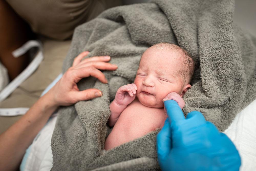 Midwife does a newborn check on twin B and hold his hand with her finger