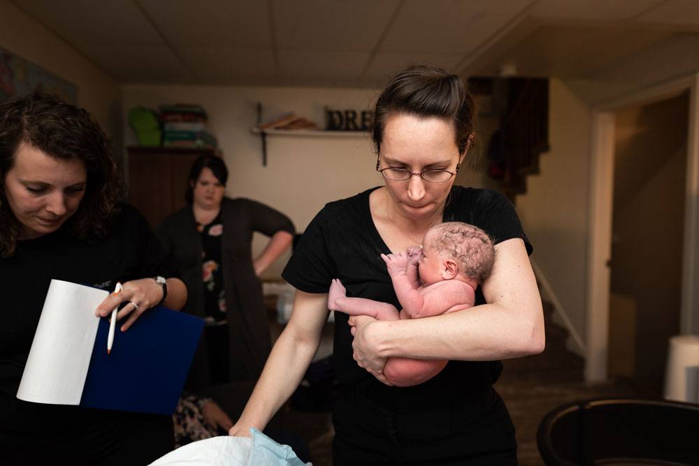 Midwife holds newborn baby boy after a home birth story