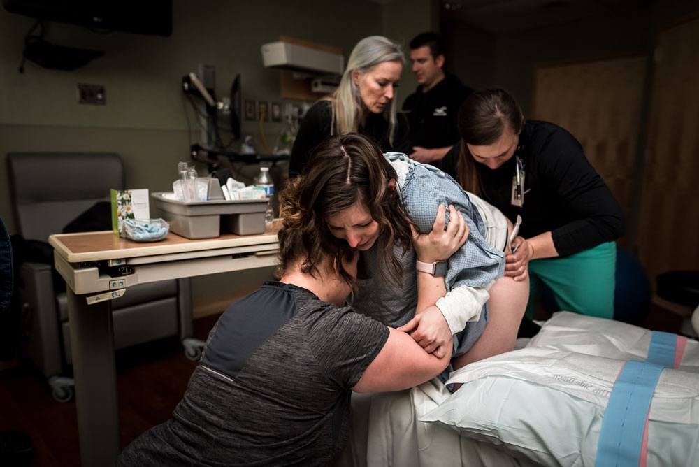 Woman works through contraction as midwife applies counter pressure and doula offers her support