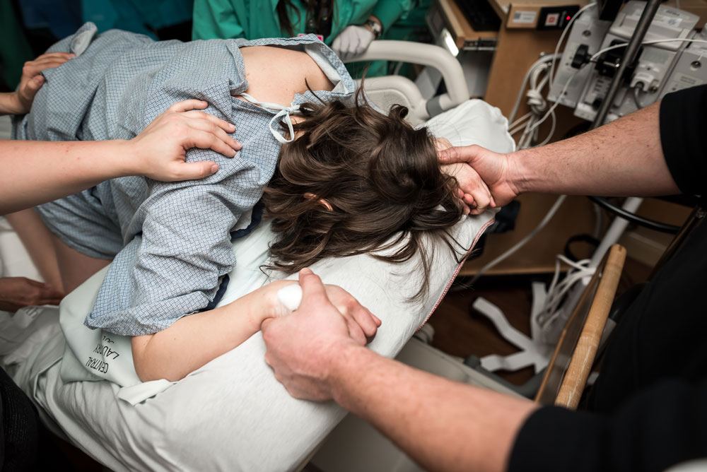 Husband holds wifes hands as she gets ready to push during the birth story photography session