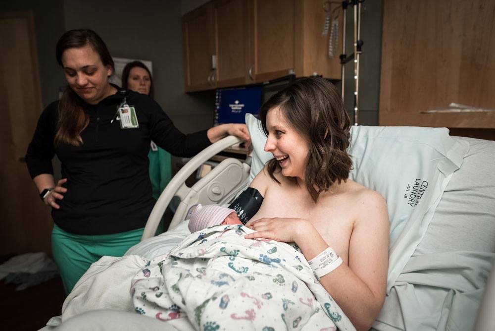 Mom smiles while breastfeeding her newborn son in the hospital bed after birth story
