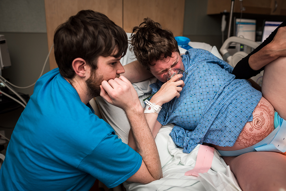 Woman pushes during labor during the birth of her newborn son while dad is close by