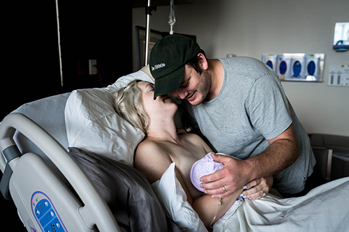 Mom and dad smile at their newborn baby girl in a hospital bed