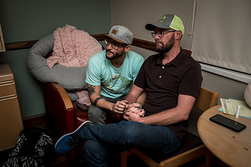 Two dads wait patiently in the hospital while they wait for their son to be born