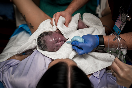 Nurse suctions the nose of a newborn baby that was placed on his mothers chest