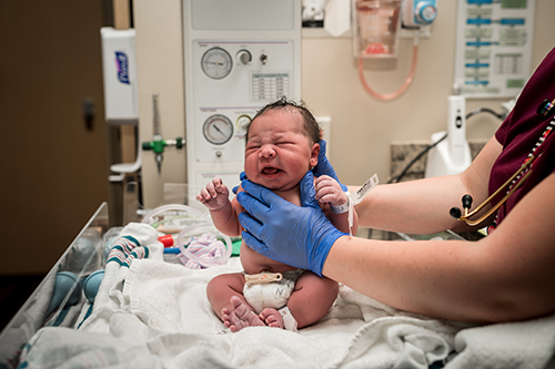 Baby is sat up on the hospital warmer, while nurse takes measurements