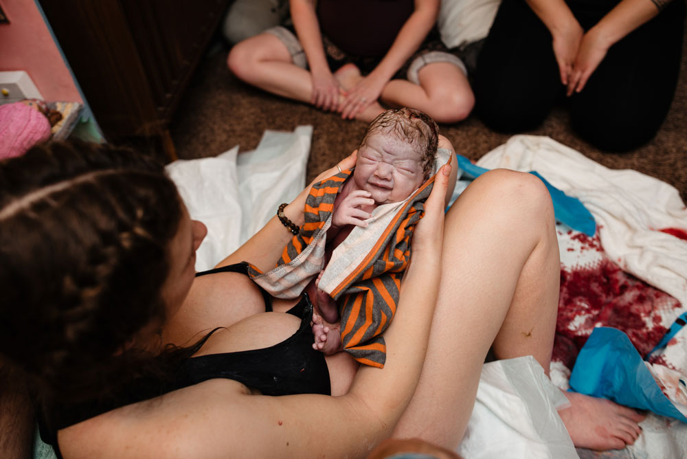 Newborn baby sits in moms hands right after birth