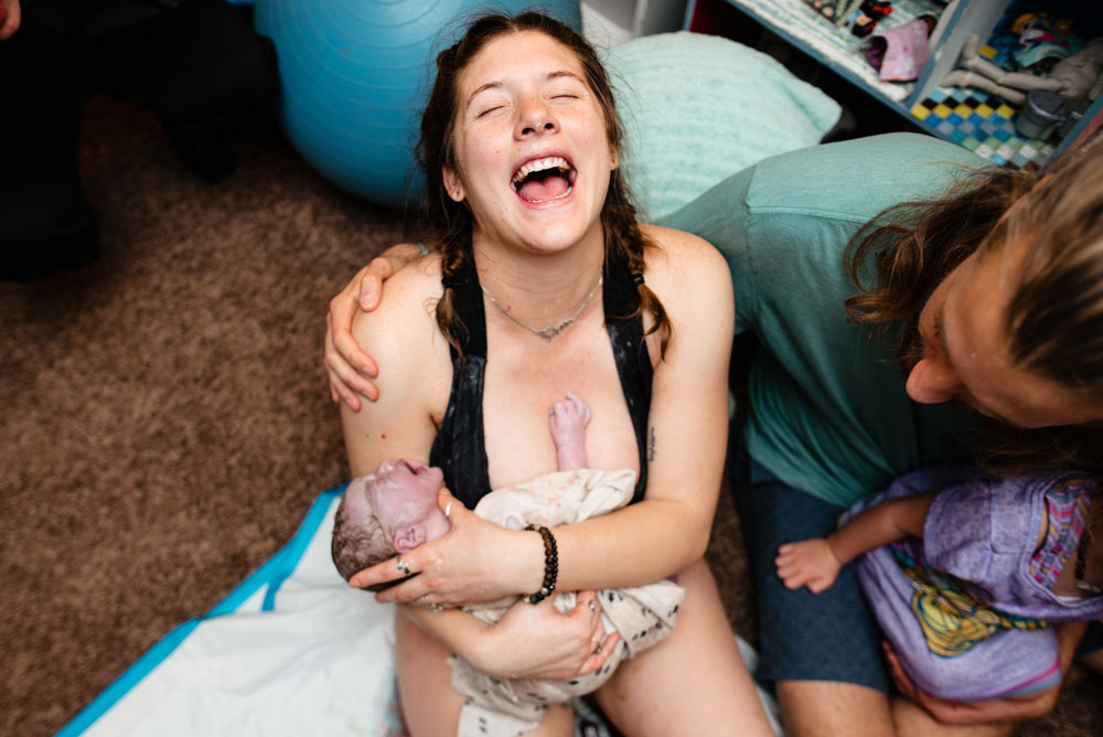 Mom laughs in joy as she holds her newborn son with her husband and daughter sitting with her