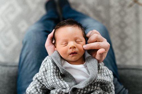 Dad touches newborn baby's face as he sleeps in his hands