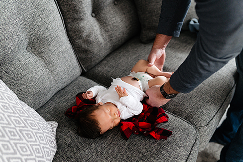 Dad changing newborn baby out of white onsie on couch
