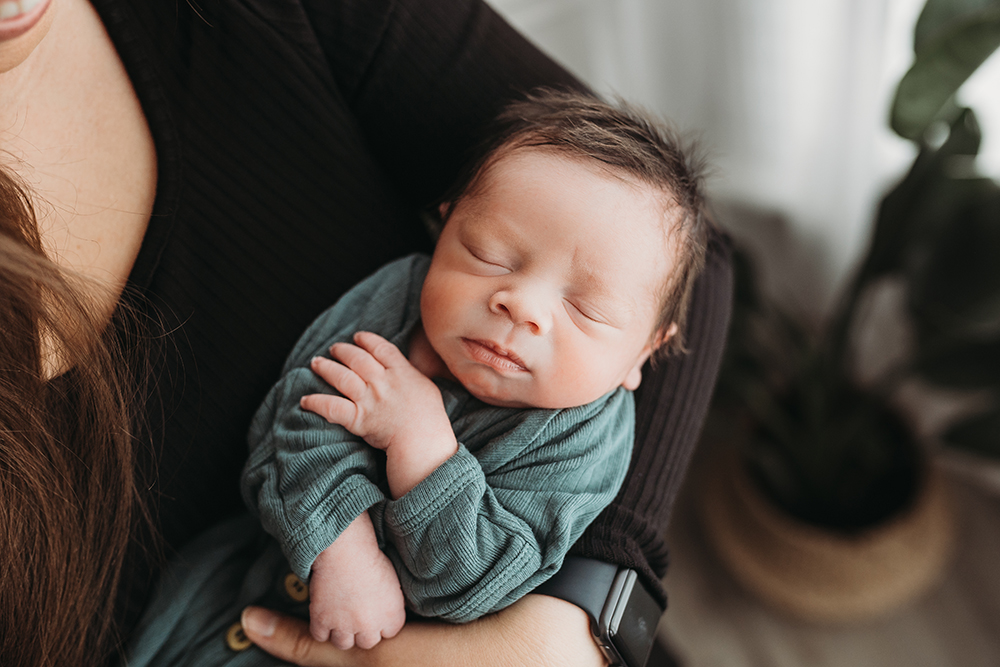 Newborn baby boy sleeps in his moms arms during lifestyle newborn session